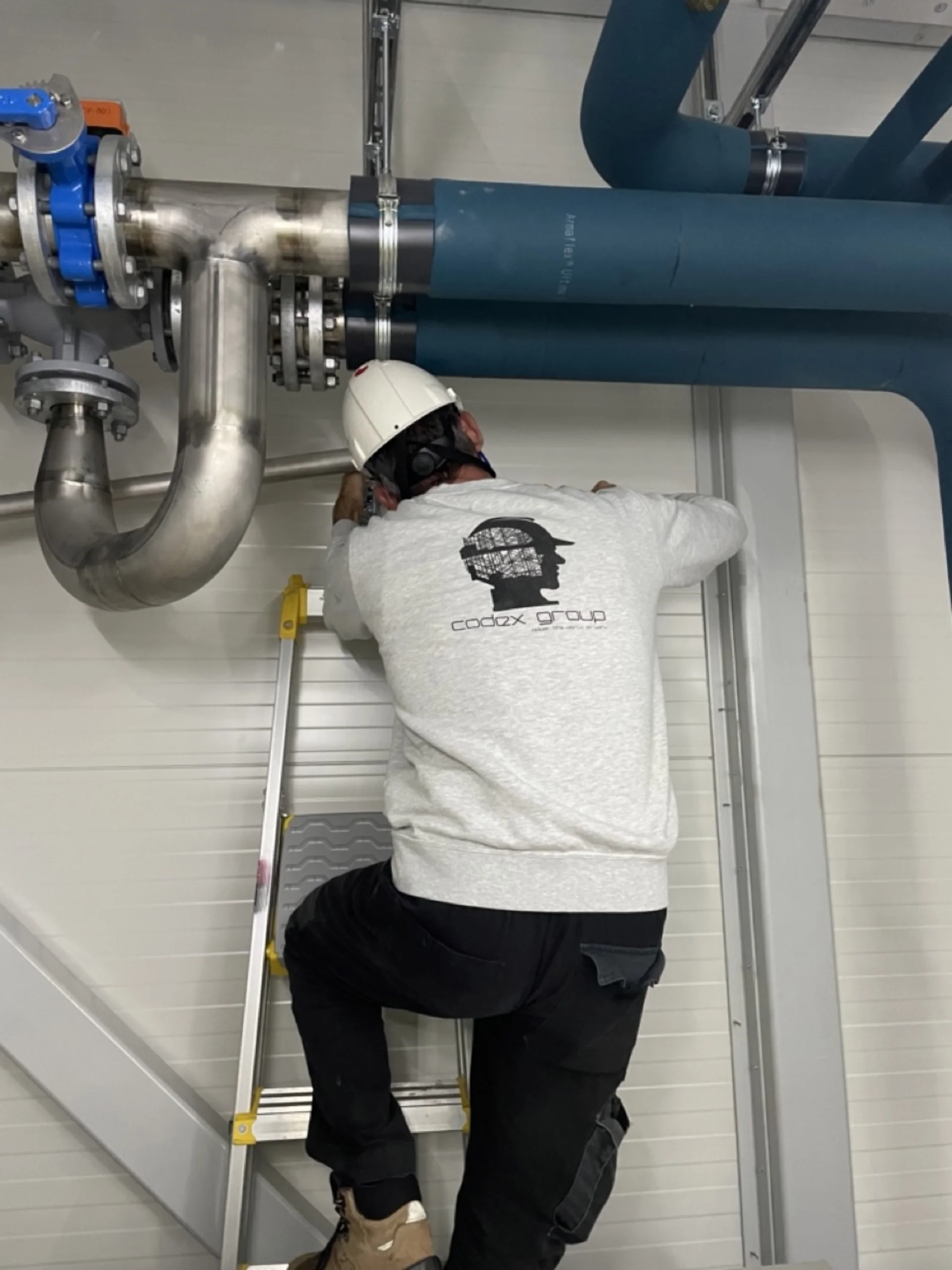 Codex Group branded worker installing industrial piping system with safety equipment